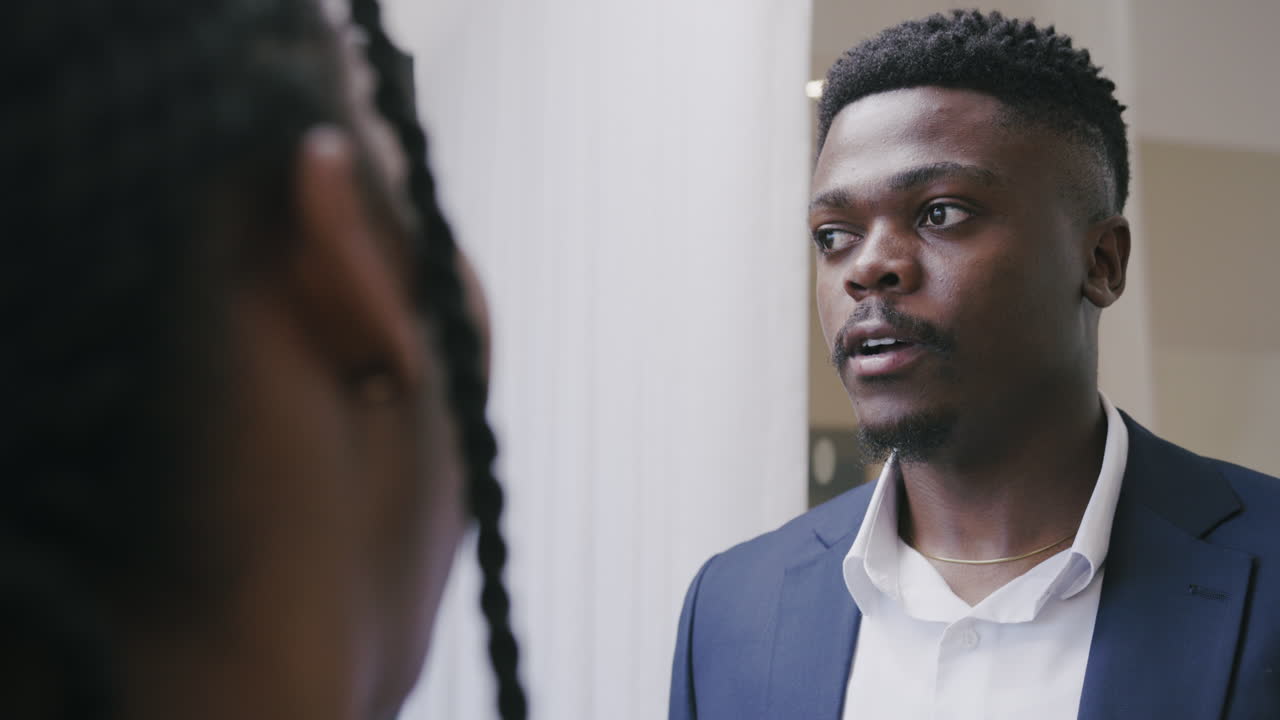 Over-the-shoulder shot of an African man talking to an African woman in a business setting, engaging in a professional discussion with clear communication