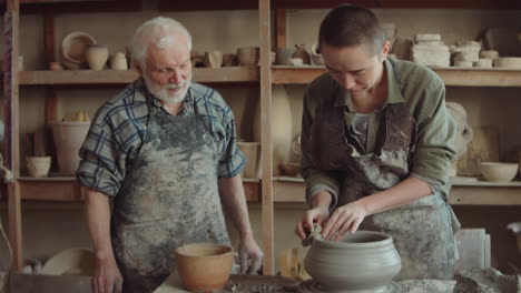 young woman learning wheel throwing with elderly potter