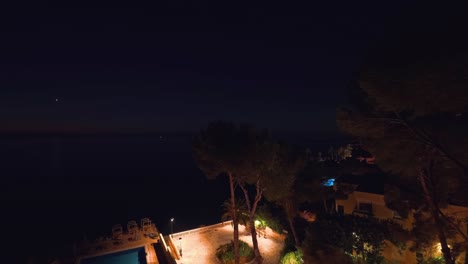 Time-lapse-drone-view-captures-a-stunning-sunrise-in-Palma-Mallorca-resort,-painting-the-sky-with-hues-of-pink,-red,-and-white,-overlooking-with-a-pool-and-swaying-trees-and-fast-waves-of-the-sea