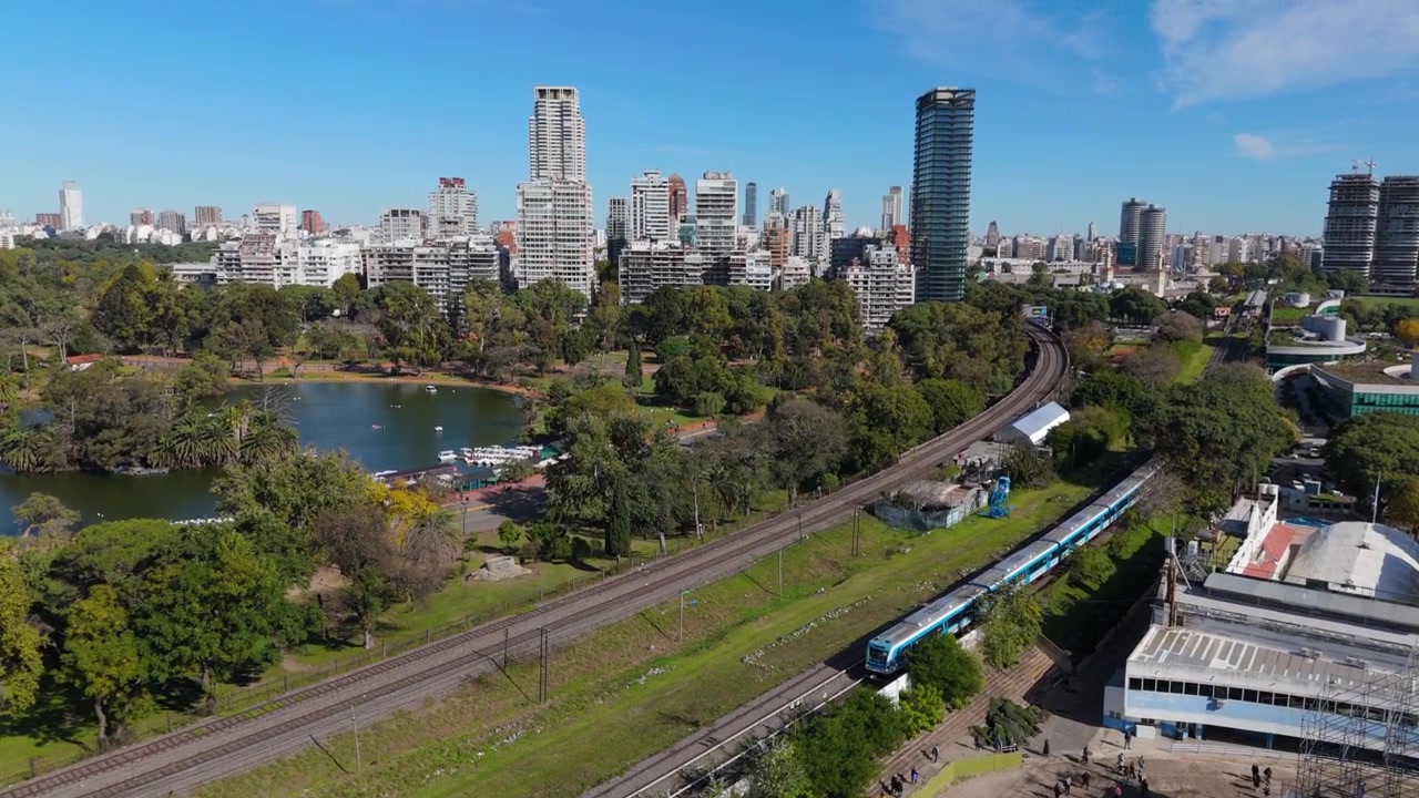 Treno passeggeri che passa davanti a un parco cittadino e allo skyline nel quartiere Palermo, Buenos Aires