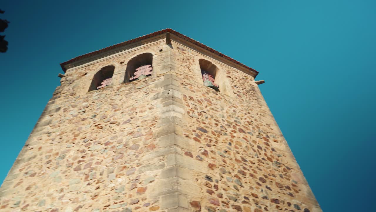 Torre campanaria pentagonale in pietra dei Templari sotto un cielo blu, in 4K.