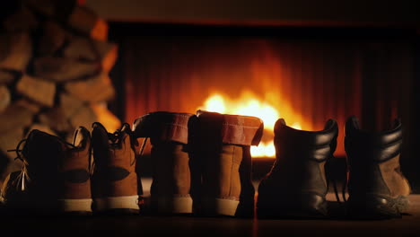 unos pares de zapatos de invierno se están secando cerca de la chimenea donde está el fuego