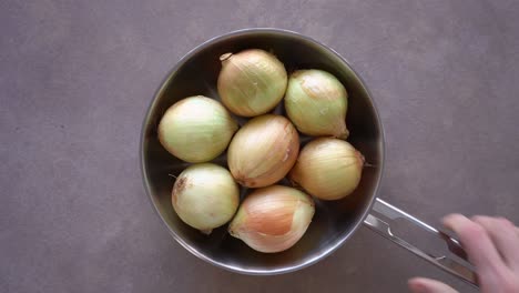 overhead view of hand put pan on the table with whole white onions