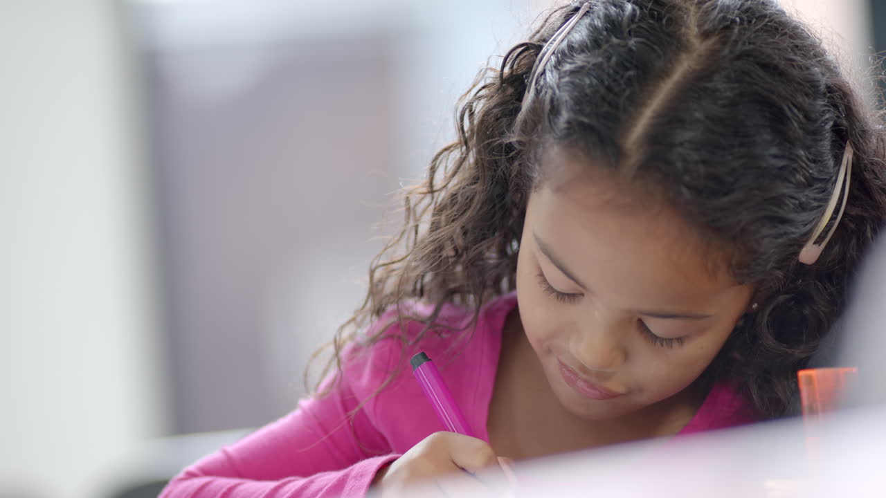 In school, in the classroom, a young biracial girl is focusing on writing