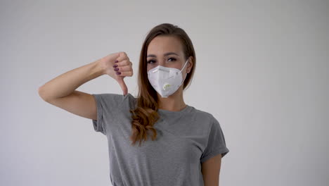 mujer joven mostrando el pulgar hacia abajo como un signo de negación o desaprobación, usando una máscara facial médica copia espacio y fondo blanco.