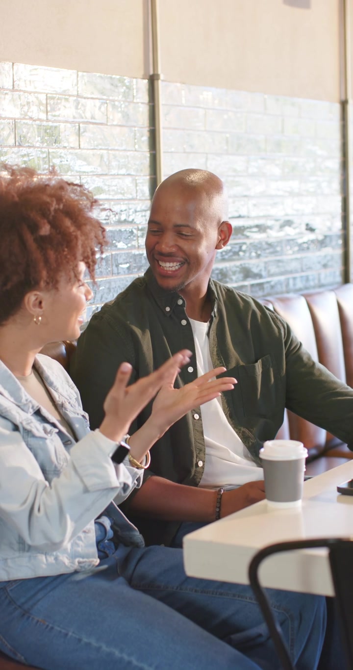 Vertical video: African American friends chatting at cafe, woman turning gesturing, man holding cup