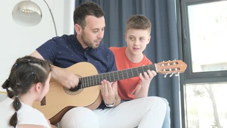 happy dad teaches his cute daughter to play the guitar while sitting on the sofa in the living room at home. happy father’s day. father teaching his child to play guitar. kid learning music skill