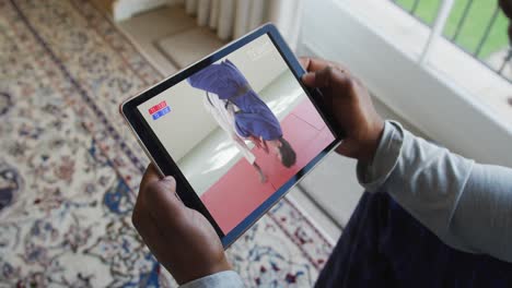 Composite-of-man-sitting-at-home,-watching-judo-match-on-tablet