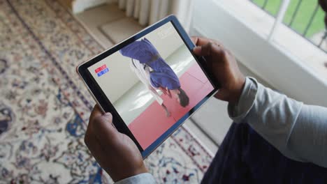 compuesto de un hombre sentado en casa, viendo un partido de judo en la tableta
