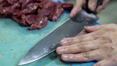 chef experto y hábilmente cortando carne roja cruda fresca con un cuchillo afilado en una tabla de corte de plástico azul