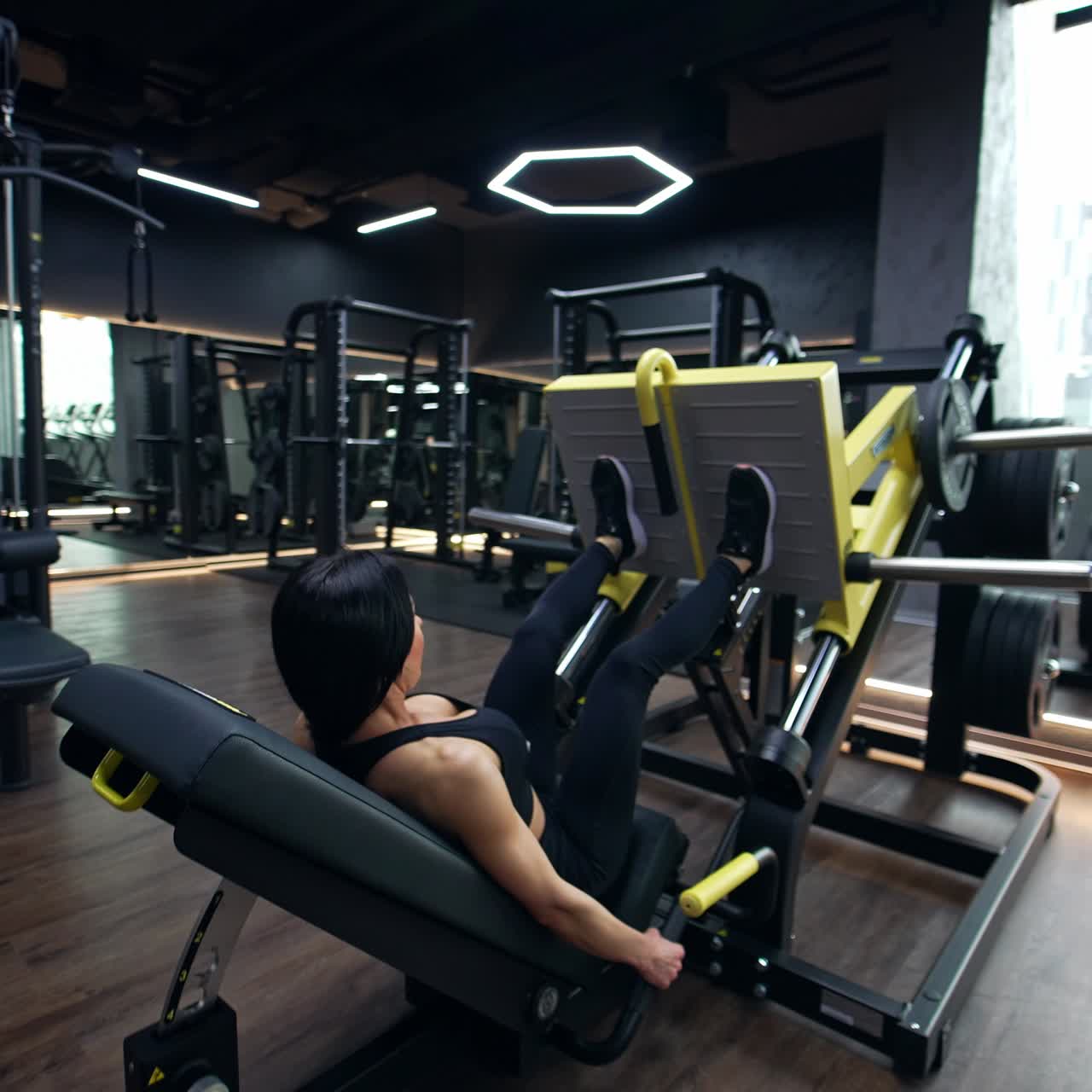 Modern sports gym almost empty. Brunette training on the simulator. Performing the exercise for leg muscles