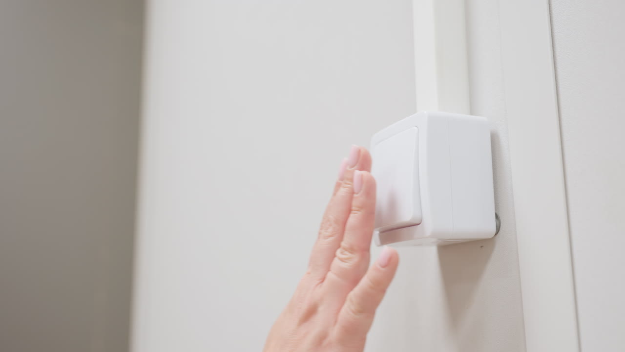 Close view of female hand pressing white wall switch with fingertips to turn off light in painted indoor room, smooth motion, clean setting, soft focus on gesture and modern minimal detail