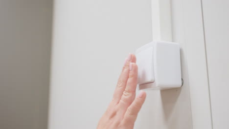 Close view of female hand pressing white wall switch with fingertips to turn off light in painted indoor room, smooth motion, clean setting, soft focus on gesture and modern minimal detail