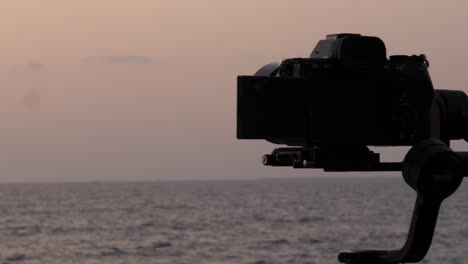 silueta de la cámara en el estabilizador de cardán filmando la puesta de sol sobre el océano