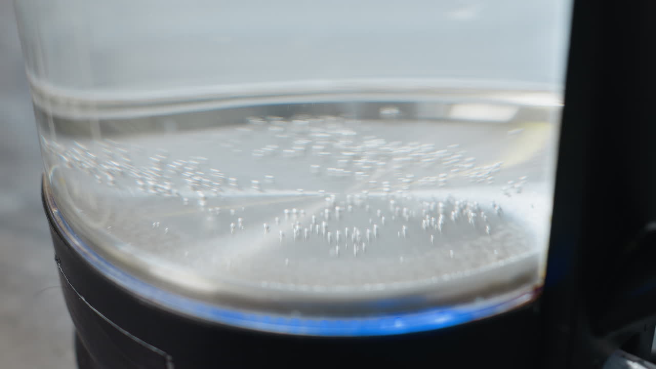 primer plano de agua hirviendo con burbujas que se elevan desde el fondo de la taza, luz azul parpadeando en la caldera de agua a medida que el líquido se calienta, movimiento visible del líquido y cambio de temperatura durante el proceso de ebullición