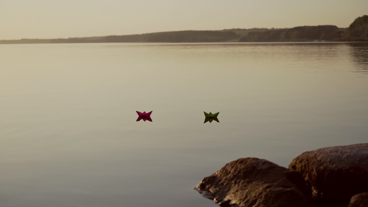 Red and green Paper Ships in the river. Origami Paper Boats are Sailing in the lake. Beautiful Waves Ripple Background. Unusual Travel Concept. Filtered video.