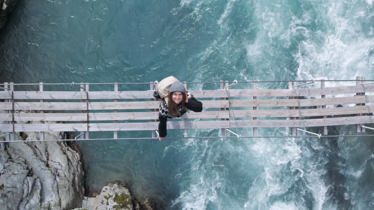 Giovane escursionista su un ponte di legno sopra una cascata.