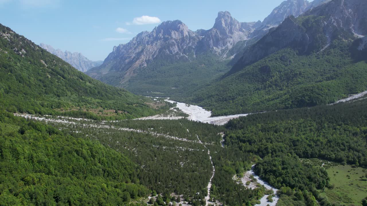 valbona valle de belleza alpina, un lecho de río meandros a través de piedras, rodeado de exuberantes bosques verdes y picos rocosos en albania