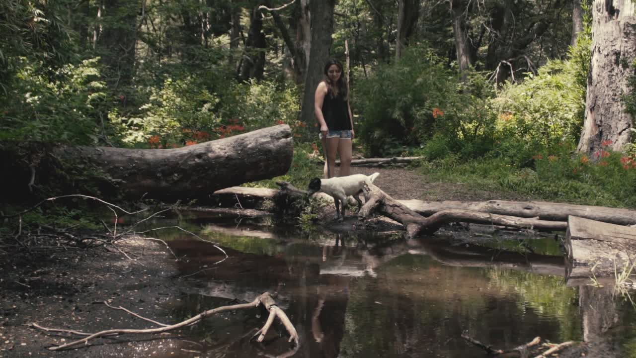 a woman waiting for her dog to drink water from the river