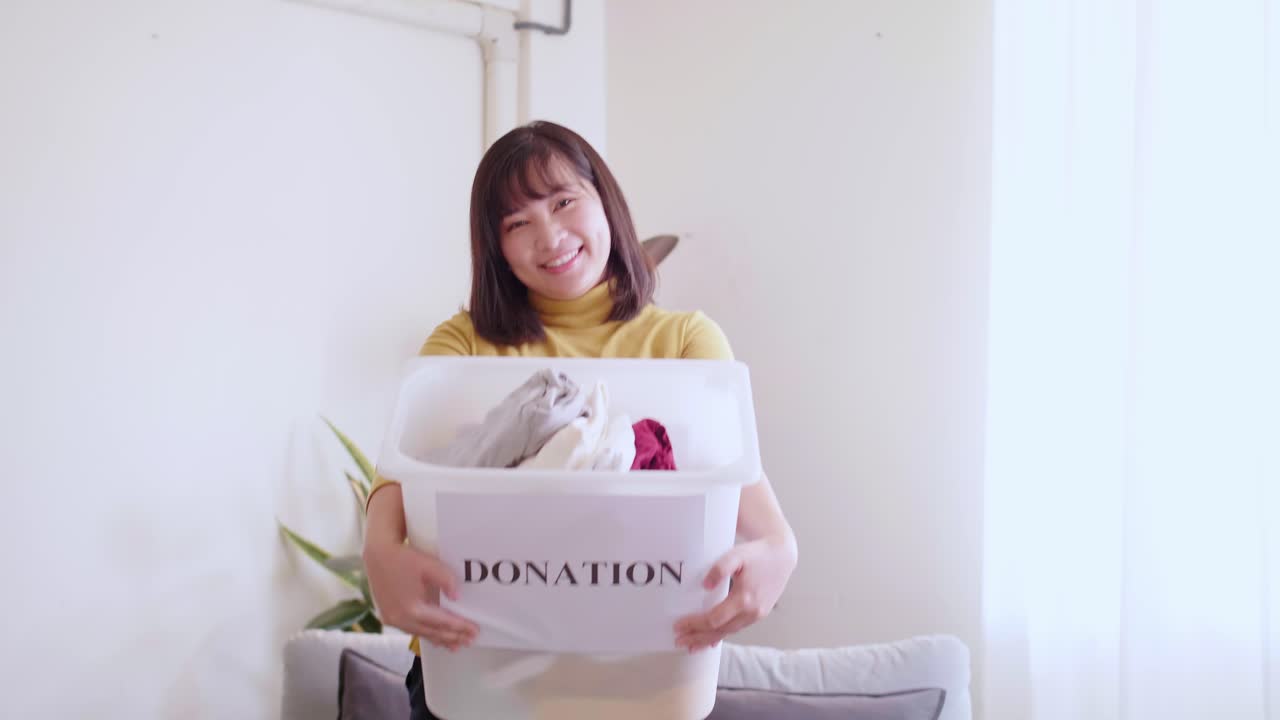 Portrait of Asian young woman looking at camera holding box with clothes for donation