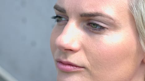 close up of white, green eyed girl with blonde hair and light make up staring off into the distance with grey background and neutral tight lipped expression