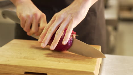 chef cuts an onion with a knife on a wooden board using clean hands, demonstrating precision and hygiene