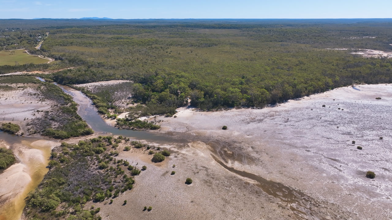 Aerial glides across diverse landscapes as Mullens Creek at Cooloola Cove meets the estuary of the Great Sandy Strait in Queensland.Vast native forests languid creeks and silver brown inlet mud flats