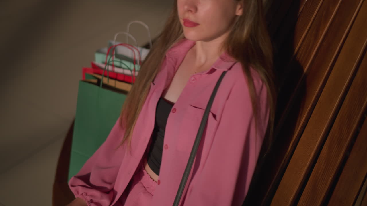 빨간색, 초록색 및 민트 녹색의 세 개의 쇼핑 가방을 가진 갈색 나무 벤치에있는 사람의 그림자, 긴장을 풀고 천천히 눈을 감고 쇼핑몰에서 평온한 순간을 즐기고있는 여성에 의해 떨어졌습니다.