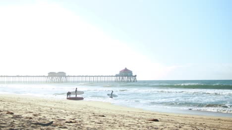 a family goes surfing at the beach during a hazy sunrise with the huntington beach pier in the background at surf city usa california