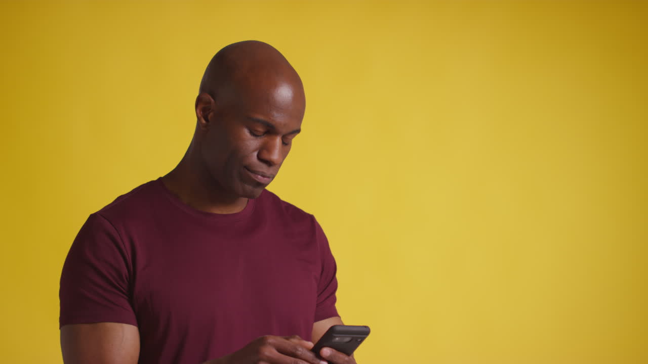 Studio Shot Of Smiling Mature Man With Mobile Phone Getting Good News Against Yellow Background 1