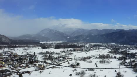 From-high-above,-the-drone's-lens-unveils-the-mesmerizing-beauty-of-Hakuba-valley-and-the-vibrant-cityscape-of-Hakuba,-painting-a-stunning-winter-picture-under-the-radiant-sunlight-of-a-clear-day