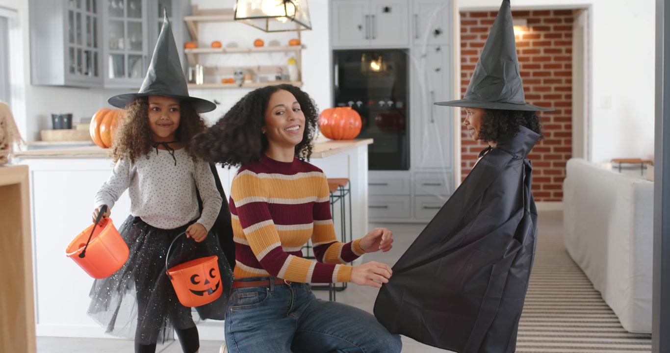 African American mom in striped top, jeans fixing costumes, giving candy from pumpkin pail at home