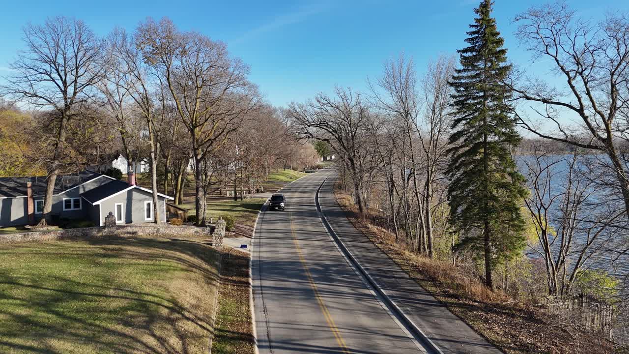 Black Truck driving down a rural road next to a lake in the Midwest. Afternoon in the late fall. Bare trees with blue skies. Southern Minnesota