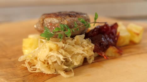 chef puts rosemary branch on plate, beef burger, cabbage, cranberry jam and roasted potatoes served on wooden board