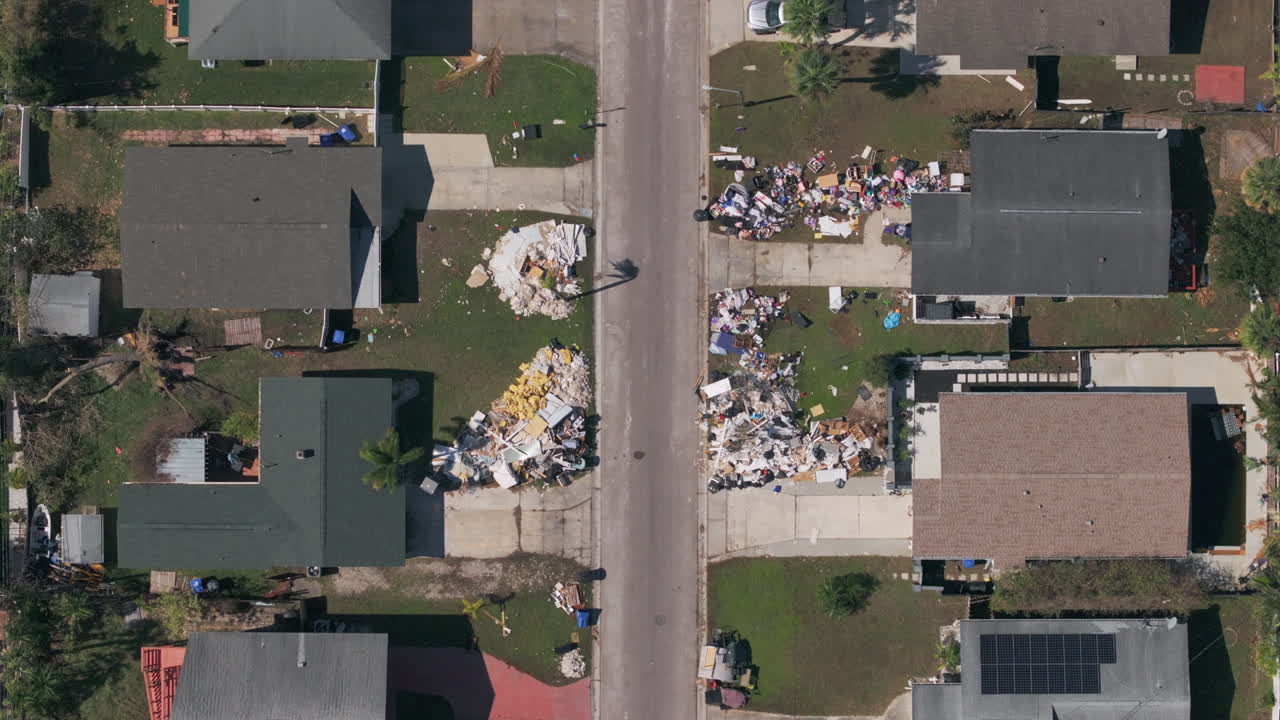 Top down drone view flying up residential Florida St. Petersburg neighborhood aftermath of Hurricane Milton destruction showing piles of trash and debris.