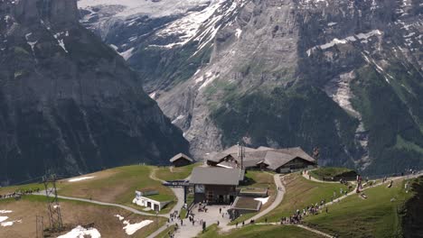 Drone-descends-tilting-up-as-cable-cars-arrive-at-the-overlook-for-Grindelwald-First,-Switzerland