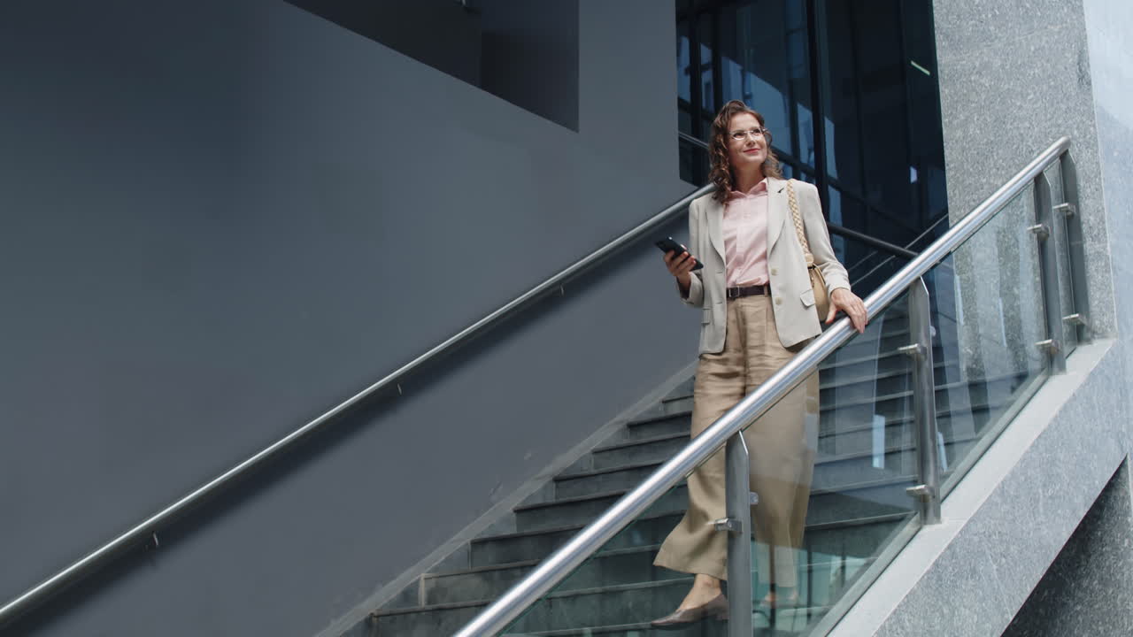 Confident Woman Looking at Phone while Going Downstairs