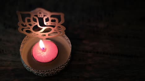Close-up of a red wax tea candle in front of Lord Ganesha golden cutout during Diwali, festival of lights, worship celebrations in dark to show the light.