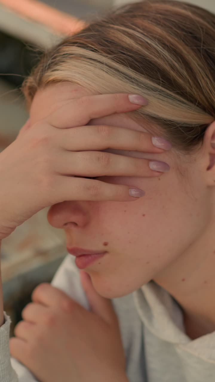 손으로 얼굴을 고 깊은 생각에 빠진 것처럼 보이는 젊은 여성의 클로즈업, 그녀는 다른 손을 팔에 고, 상적인 분위기를 발산합니다.