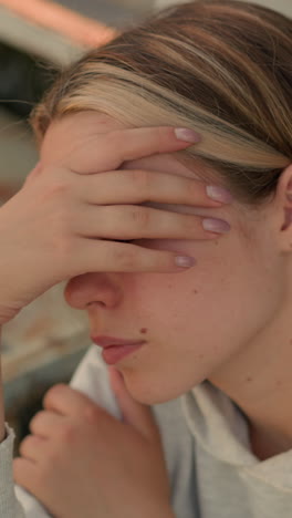 primer plano de una mujer joven cubriendo su rostro con su mano, apareciendo profundamente en pensamiento, ella descansa su otra mano en su brazo, emanando un estado de ánimo contemplativo, el fondo muestra pasos desgastados