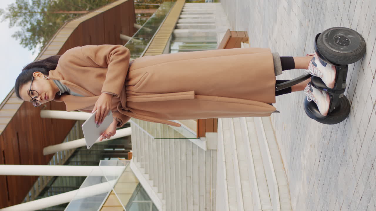 A woman stands on a hoverboard while looking at a tablet outdoors