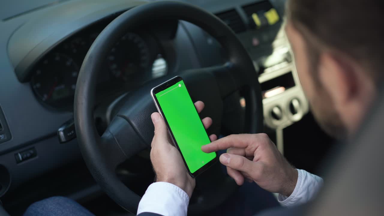 hombre con la mano deslizando la pantalla verde del teléfono inteligente en el volante del coche. joven caucásico borroso navegando por internet en las redes sociales sentado en el asiento del conductor en el vehículo. estilo de vida y tecnologías modernas.