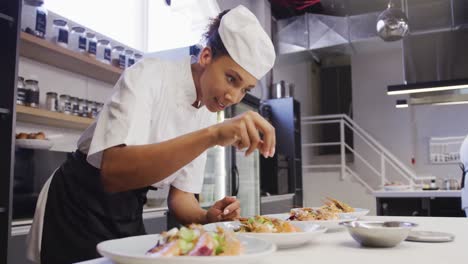 African-American-female-chef-wearing-chefs-whites-in-a-restaurant-kitchen,-putting-food-on-a-plate