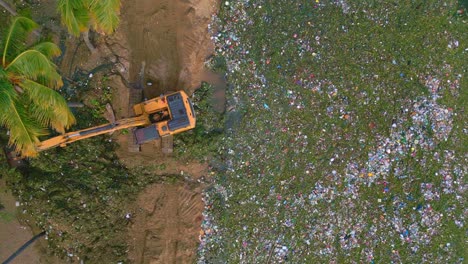 excavator digging garbage and bottles out of caribbean sea shoreline at playa montesinos - environmental pollution on tropical island of dominican republic - aerial straight down