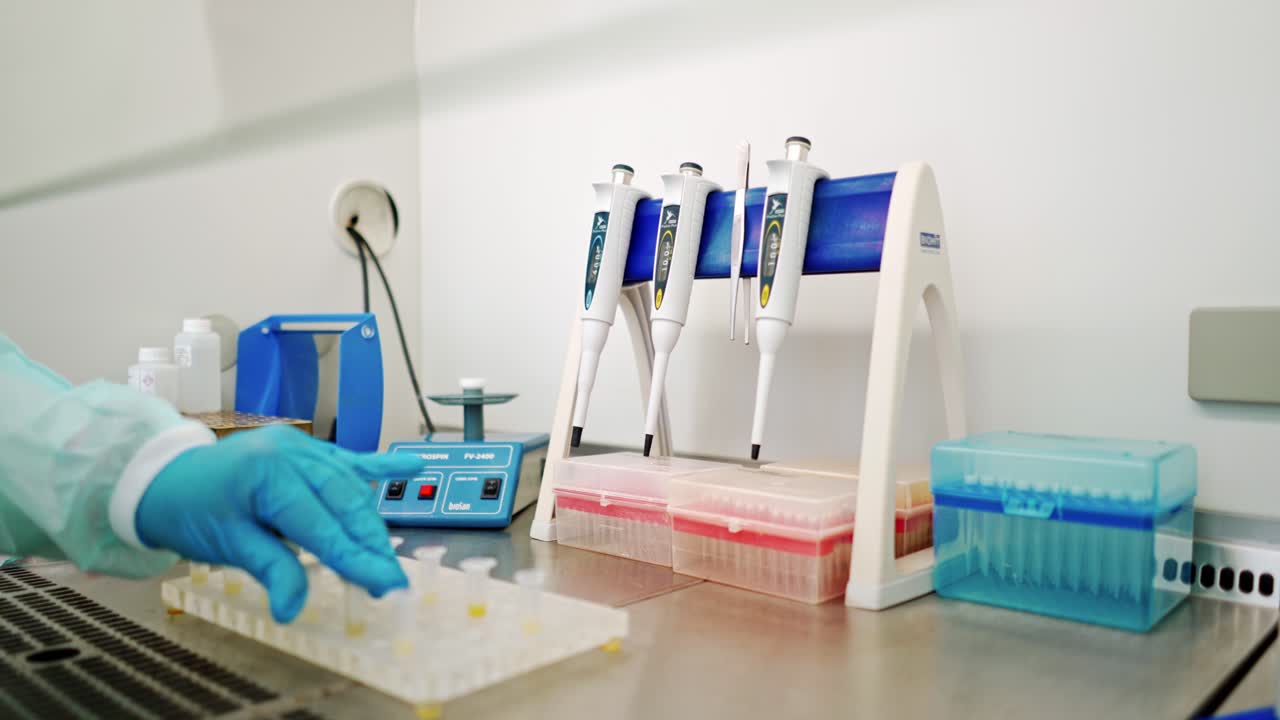 Hand of medical worker checking vials of liquid. Female's hand in sterile glove putting test tubes one by one into special machine in lab.