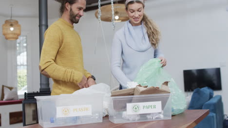 pareja diversa segregando botellas de plástico y papel en casa, en cámara lenta