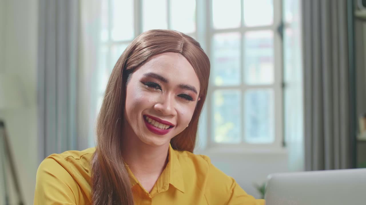 Asian Young Transgender Woman Working With Laptop Computer And Smiling To Camera In Living Room