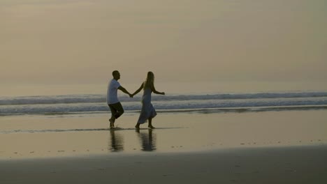 Cinematic-shot-of-happy-Caucasian-couple-running-along-seashore.