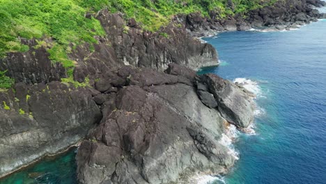 órbita-Aérea-De-Rocas-Basálticas-Afiladas-A-Lo-Largo-De-Una-Isla-Tropical-Con-Exuberante-Vegetación-Y-Aguas-Turquesas-Del-Océano