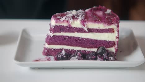 person eating a slice of purple red velvet cake with blueberries